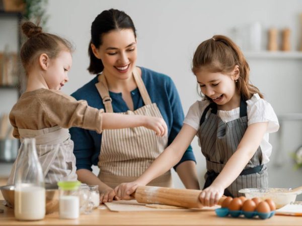 Happy loving family are preparing bakery together. Mother and children daughters girls are cooking cookies and having fun in the kitchen. Homemade food and little helper.